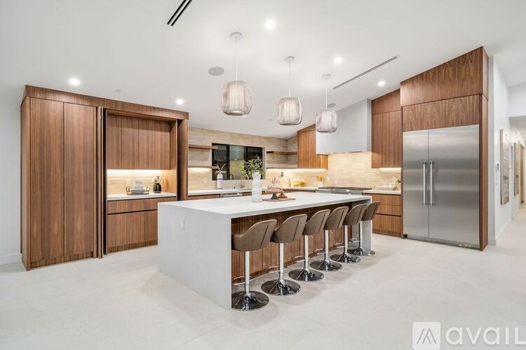 A modern kitchen with a long white island and dark wood cabinets.