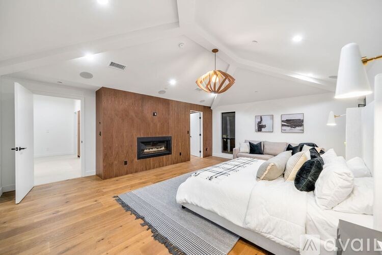 A bedroom with a fireplace and a bed with a white comforter.