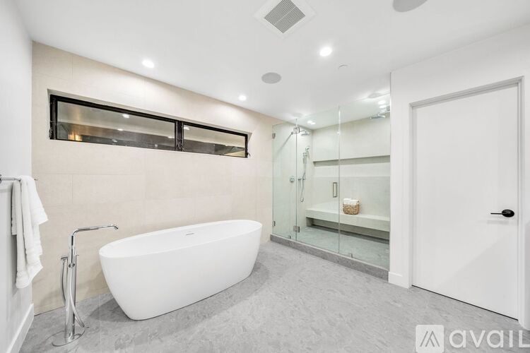 A modern bathroom with a white freestanding bathtub and a glass shower enclosure.