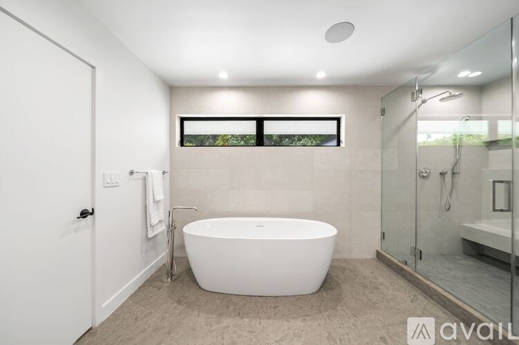 A modern bathroom with a white freestanding bathtub and a glass shower enclosure.