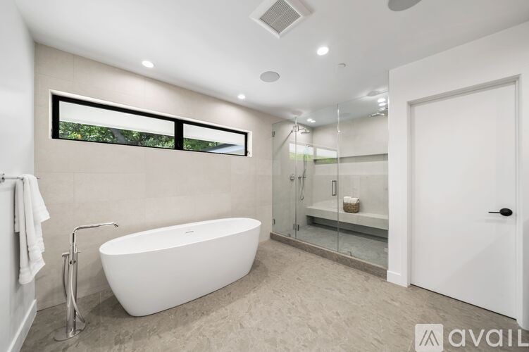 A modern bathroom with a white freestanding bathtub and a glass shower enclosure.
