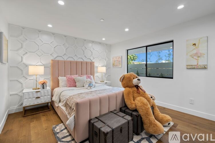 A bedroom with a large bed and a teddy bear sitting on a bench.