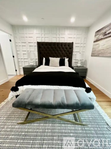 A bedroom with a black headboard and a grey bench.