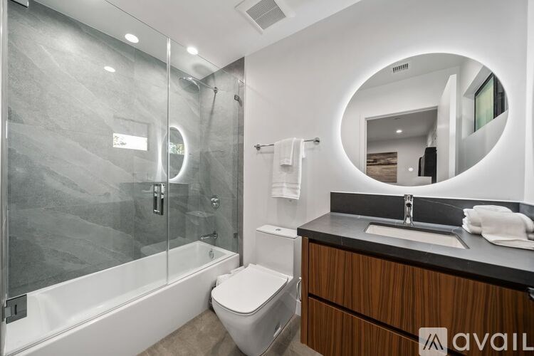 A modern bathroom with a glass shower enclosure and a round mirror.