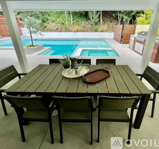 A wooden table with chairs and a tray on it with a pool in the background.