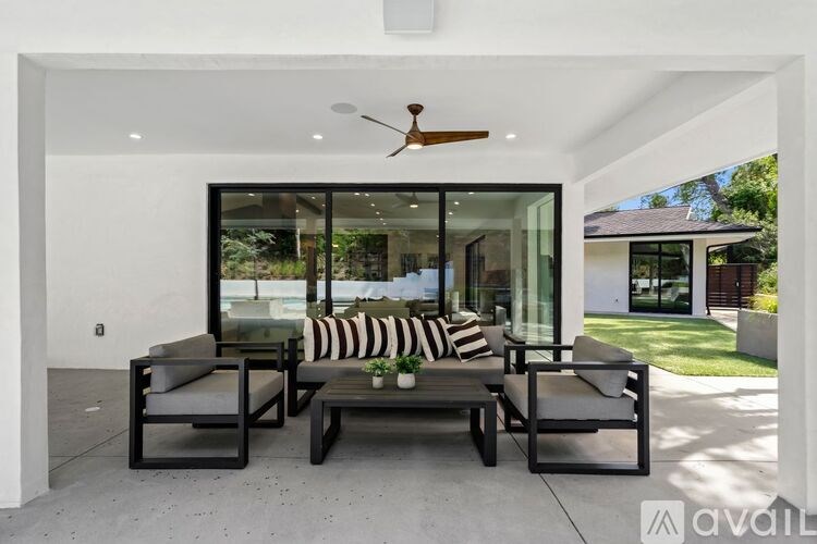 A modern outdoor seating area with a ceiling fan and a view of the backyard.