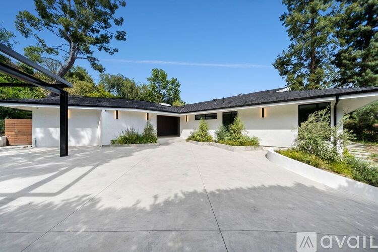 A modern house with a large driveway and trees in the background.