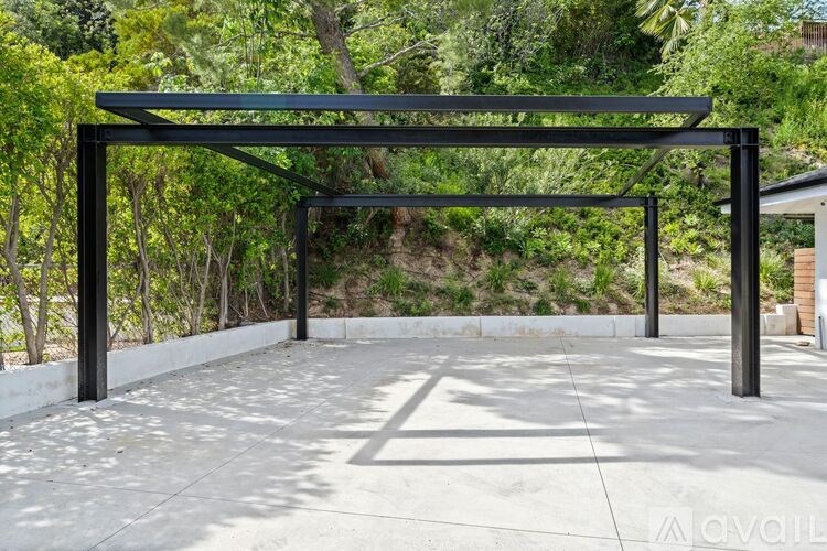 A black metal structure is situated in a concrete courtyard with trees in the background.