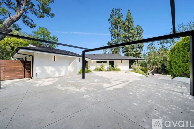 A house with a white exterior and a black roof is surrounded by trees and has a concrete driveway.