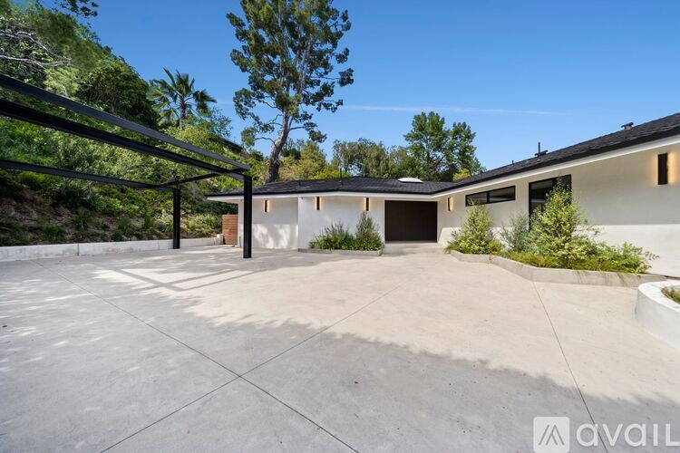 A modern house with a large driveway and a tree in the background.
