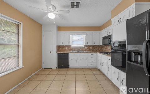 A kitchen with white cabinets and appliances, a window with blinds, and a ceiling fan.