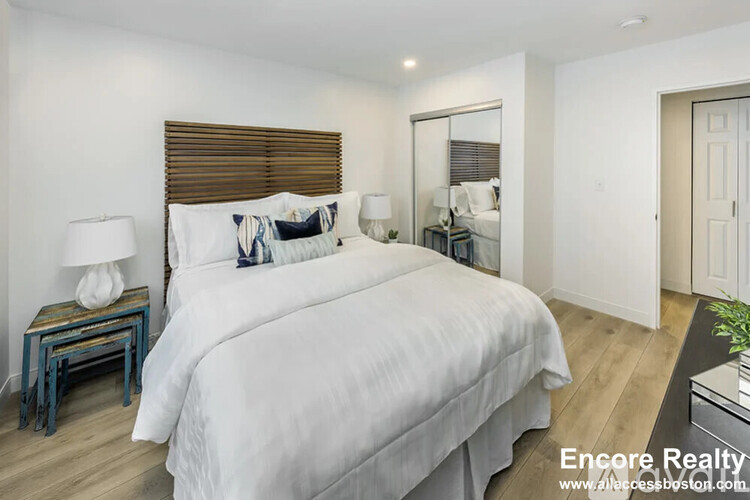 A bedroom with a large bed, a nightstand with a lamp, and a mirror on the wall.