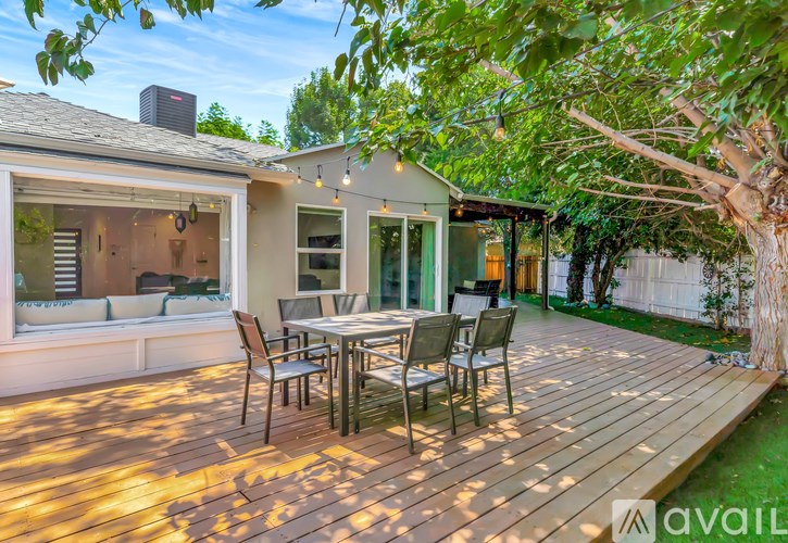 A wooden deck with a table and chairs is surrounded by greenery.