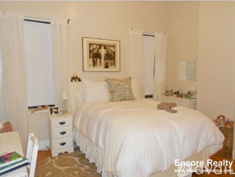 A white bedroom with a large bed and a teddy bear on it.