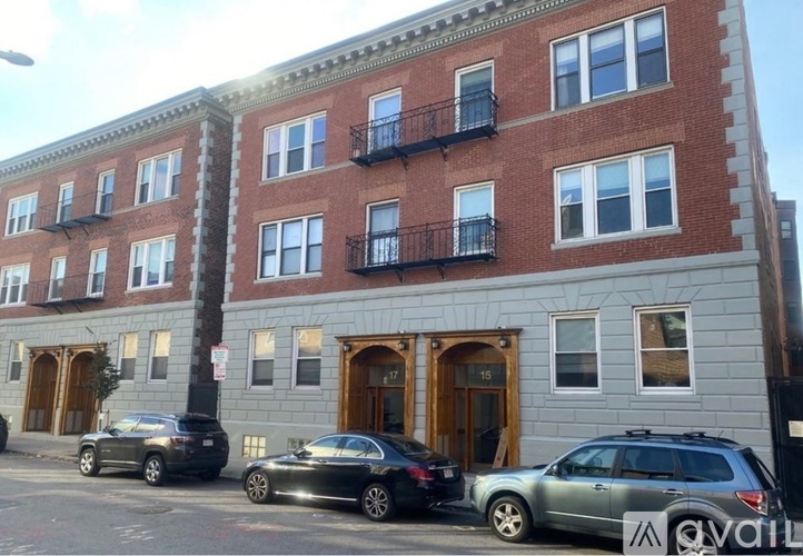 A row of red brick buildings with balconies and cars parked in front.