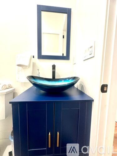 A blue cabinet with a bowl sink and a mirror above it.