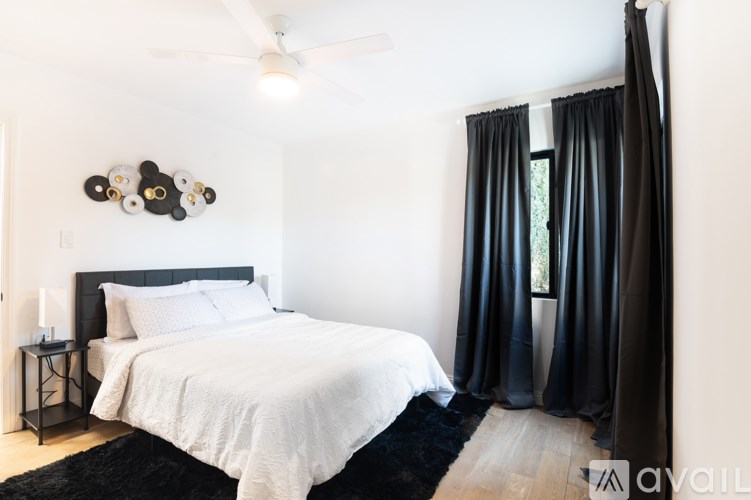 A bedroom with a white bed and black curtains.