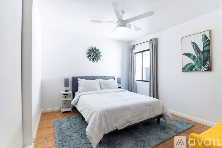 A bedroom with a bed, a ceiling fan, and a painting on the wall.