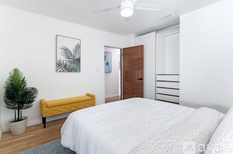 A bedroom with a bed, a bench, and a plant.