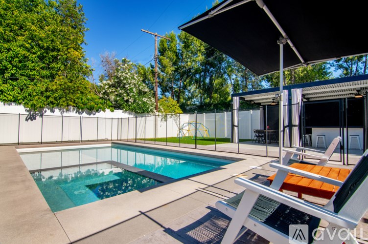 A pool with a glass fence and a patio with chairs.