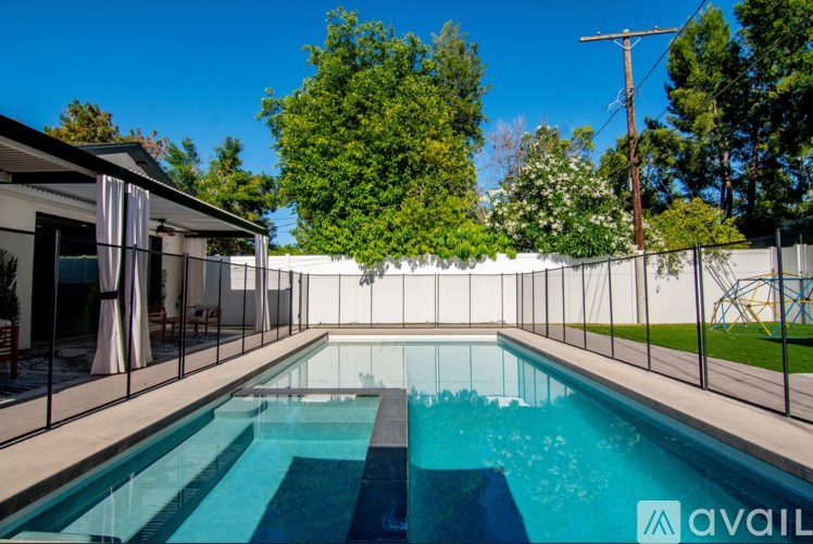 A pool surrounded by a fence with a house and trees in the background.