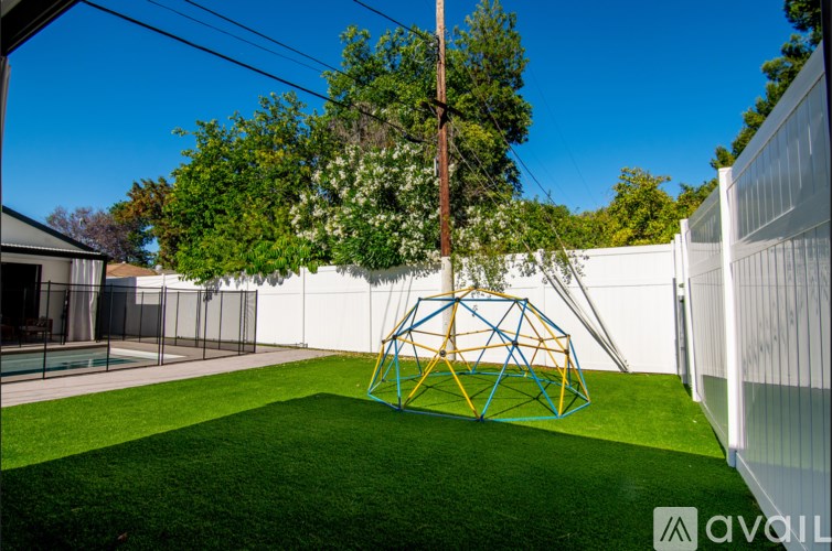 A playground with a yellow and blue pyramid-shaped structure in the middle of a green lawn.