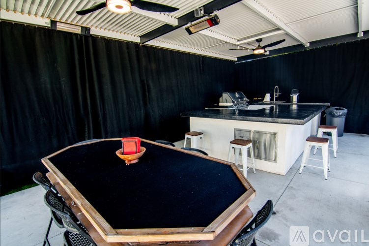 A poker table with a red card holder on it is in the foreground of a room with a kitchen in the background.