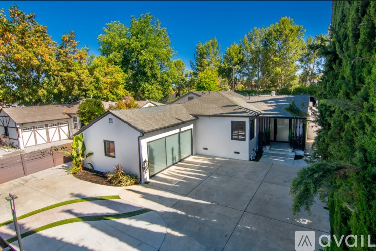 A house with a white exterior and a grey roof is surrounded by trees.
