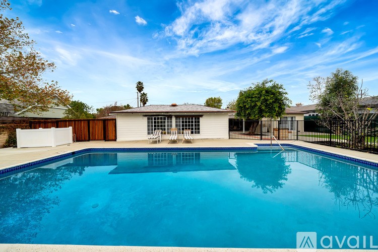 A swimming pool in front of a house with a fence and trees.