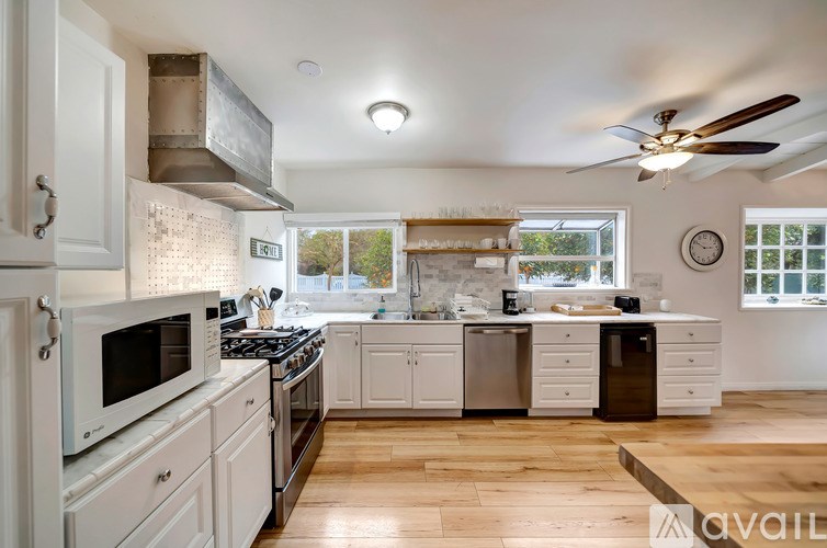 A kitchen with white cabinets and appliances, a wooden floor, and a ceiling fan.