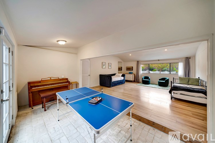 A blue ping pong table is in the middle of a room with a piano, a couch, and a bed.