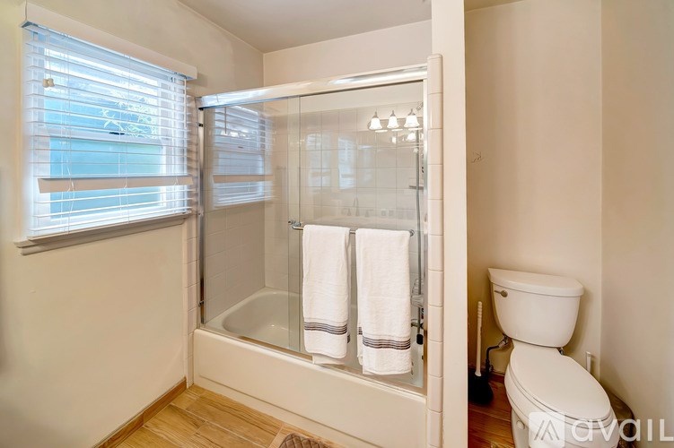 A bathroom with a toilet, a window with blinds, and a glass shower door.