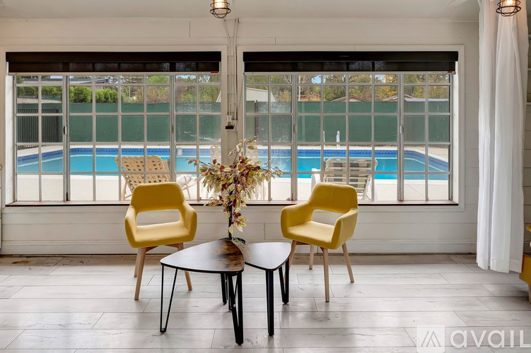 A table with two chairs and a vase of flowers in front of a window with a pool in the background.