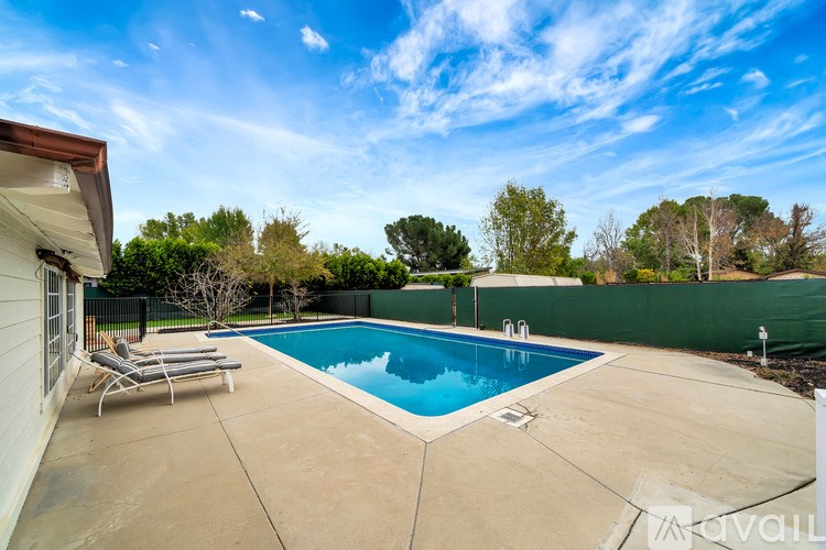 A swimming pool in a backyard with a sun lounger and a house.