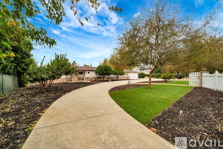 A concrete pathway leads through a landscaped yard with a white fence and houses in the background.
