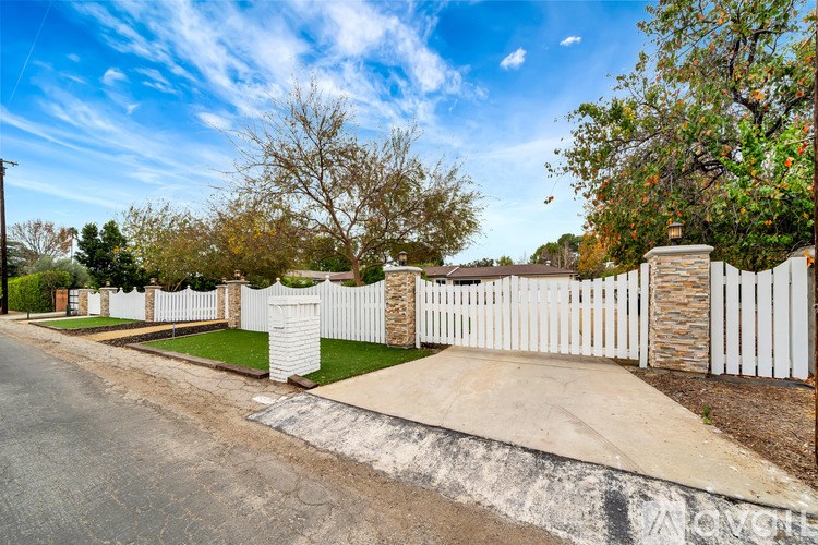 A street view with a white picket fence and a stone pillar.