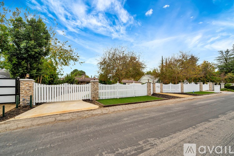 A residential street with a white picket fence and houses on both sides.