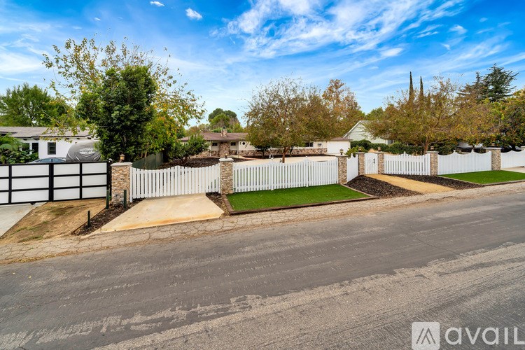 A residential street with houses and a white fence.