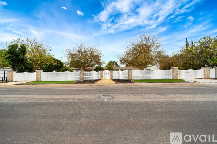 A white fence surrounds a tree-lined street.