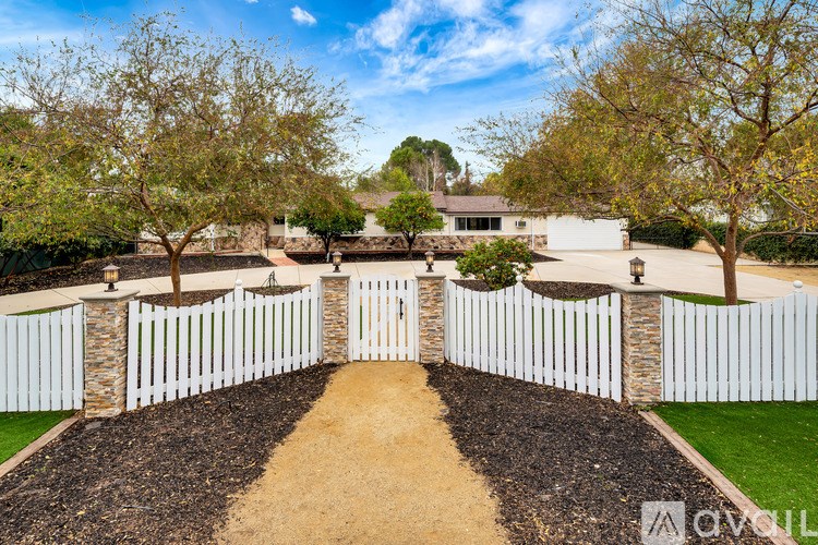 A white fence surrounds a house with a driveway leading to the front door.