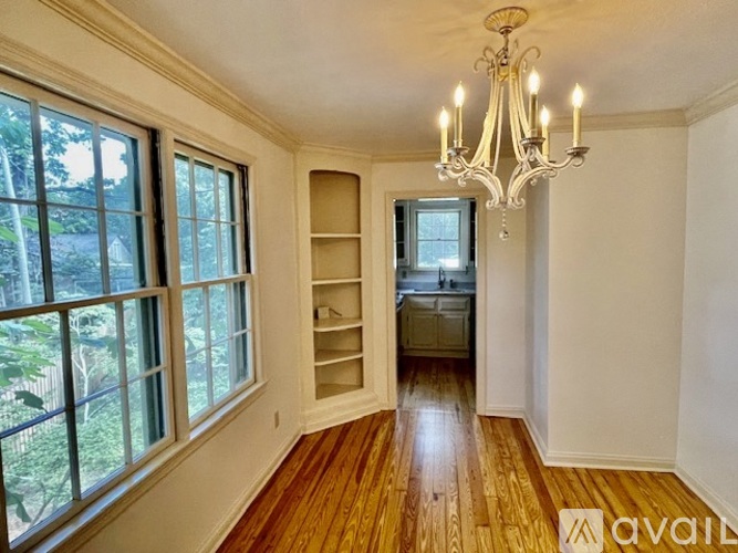 A room with a chandelier, wooden floors, and a large window with a view of trees.