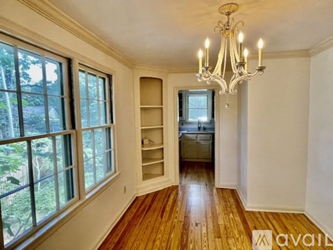 A room with a chandelier, wooden floors, and a large window with a view of trees.
