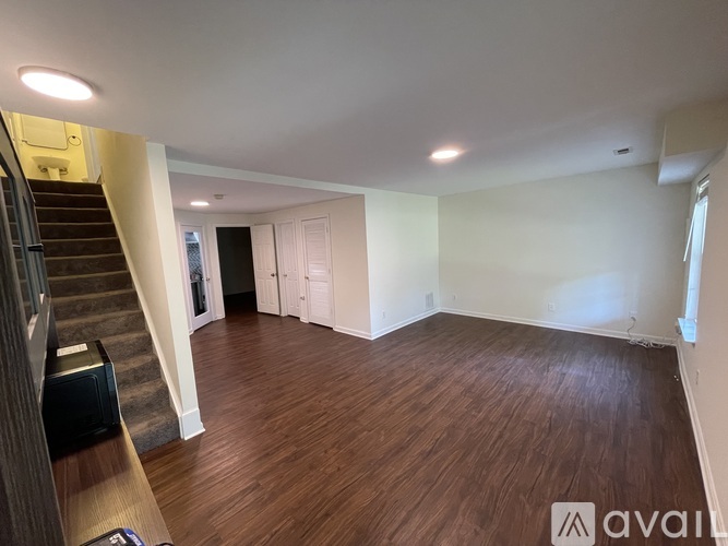 A spacious room with wooden flooring and a staircase on the left side.