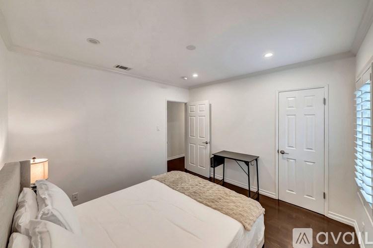 A bedroom with a bed, desk, and two doors.