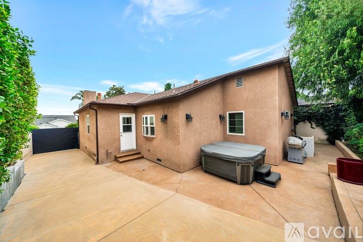A house with a brown roof and a white door is surrounded by a fence and has a hot tub in the backyard.