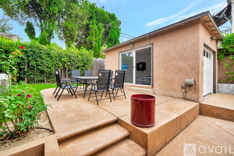A patio with a table and chairs is surrounded by greenery.
