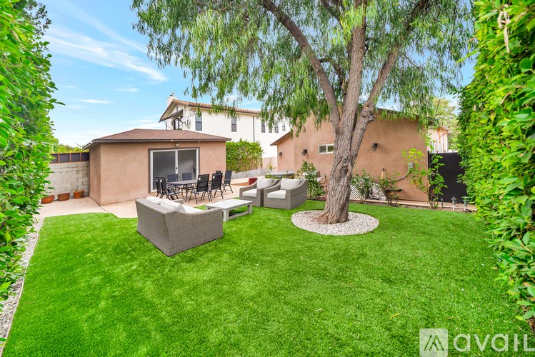 A backyard with a tree, a patio, and a lawn.