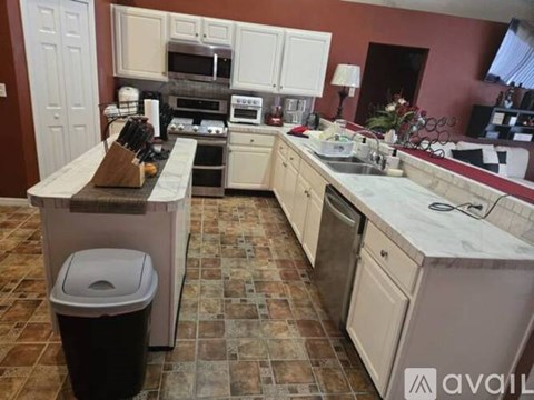 A kitchen with brown tiles and a white trash can.