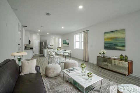 A modern living room with a black leather couch, a glass coffee table, and a painting on the wall.