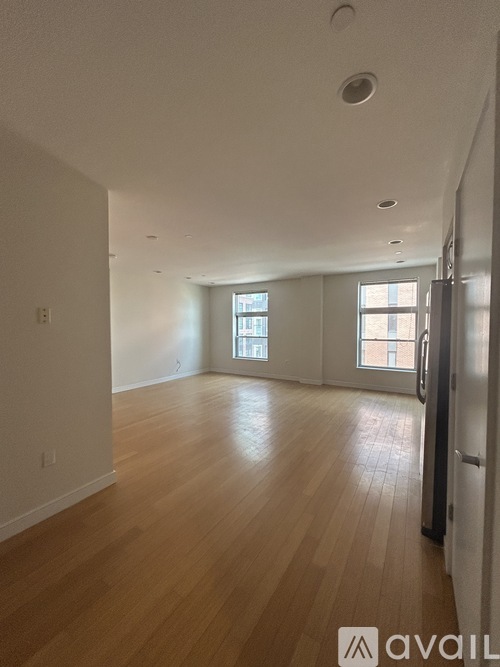 A spacious room with wooden flooring and a refrigerator on the right side.